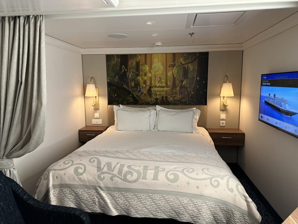 Inside a Disney Wish stateroom with a queen bed and soft neutral decor