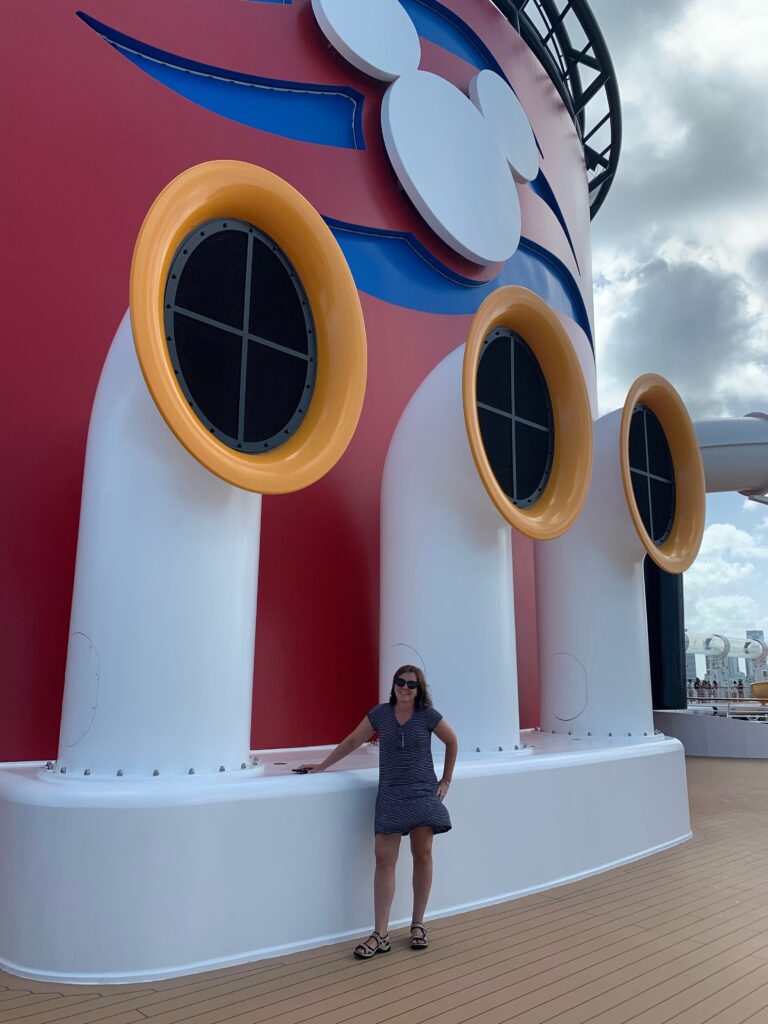 Travel advisor standing beside the Disney Cruise Line funnel aboard a Disney ship